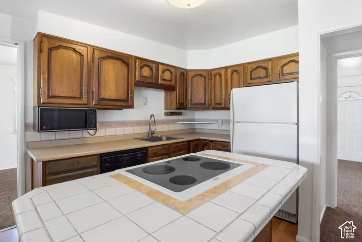 Kitchen featuring wood-finish cabinetry, tile backsplash, laminate countertops, and a tile-top island with an integrated cooktop