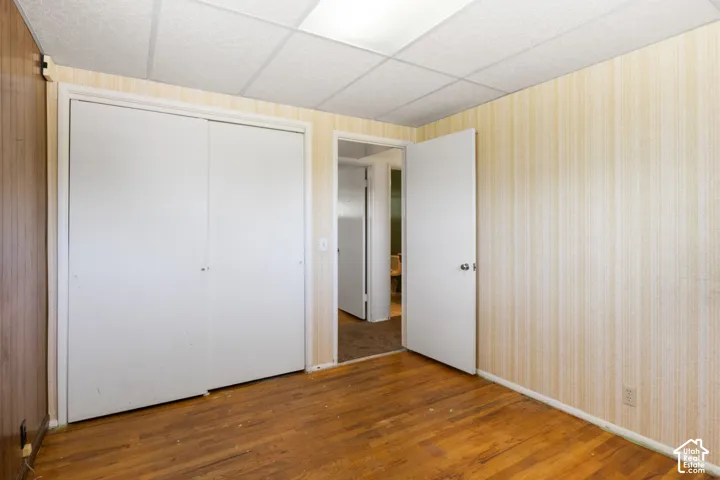 Wood-finish flooring, white bi-fold closet doors, textured wall covering, and a drop ceiling with recessed lighting
