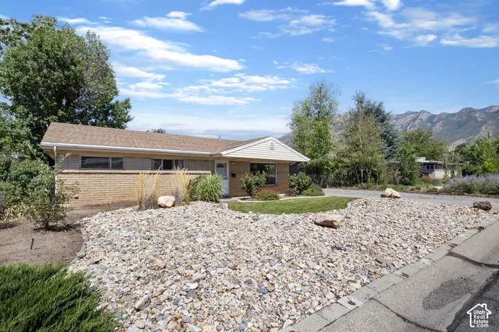 Brick and siding exterior with a pitched roof, gravel landscaping, and established trees