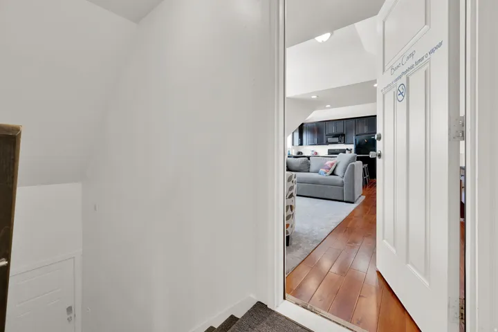 Rich wood-finish flooring leads into an open living area with dark cabinetry, stainless steel appliances, and recessed lighting