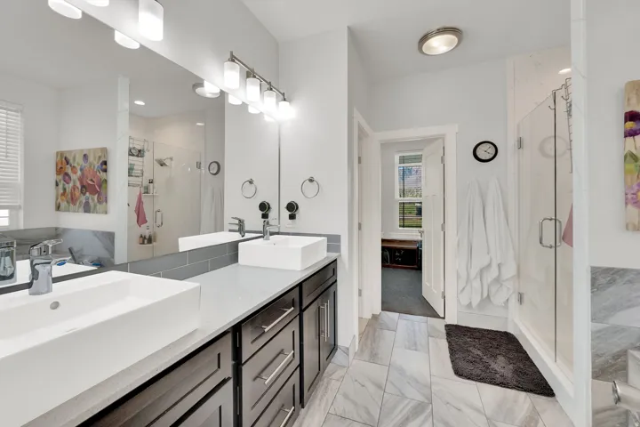 Double vanity with vessel sinks, dark wood-finish cabinetry, light gray countertop, full-height mirror, and a glass-enclosed shower