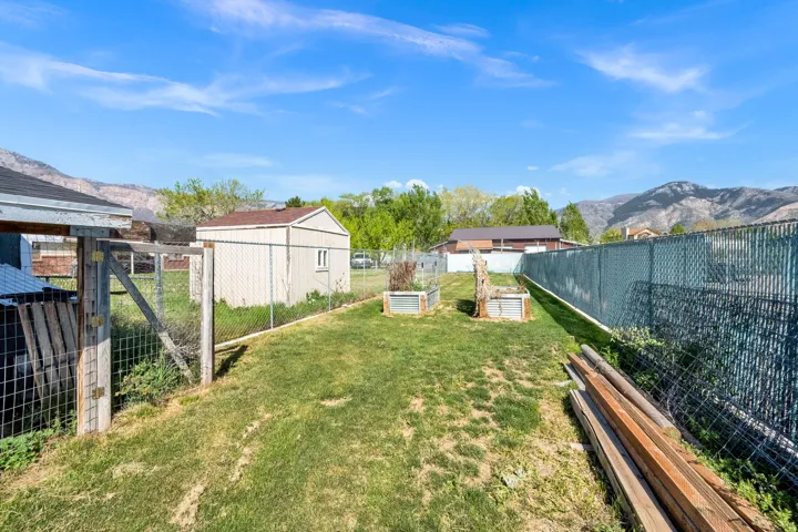 Expansive backyard featuring a storage shed, raised garden beds, and mountain scenery