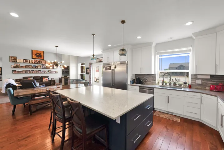 Spacious kitchen with a large island, white cabinetry, integrated stainless steel appliances, and wood-finish flooring