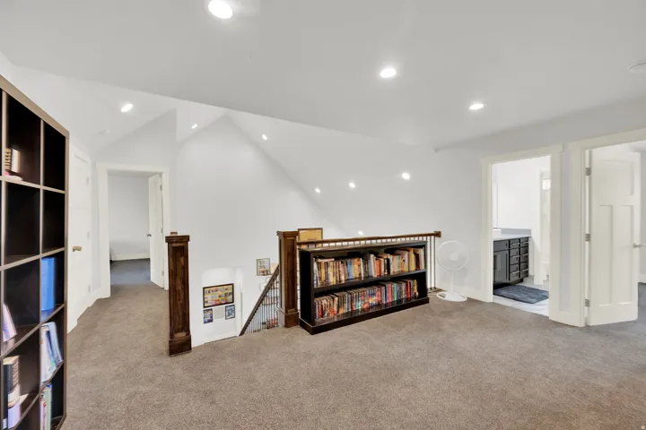 Carpeted room with recessed lighting, white walls, and a wood banister