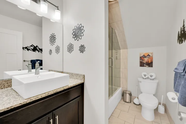 Vessel sink with a granite-style countertop, dark wood-finish vanity, and a glass-enclosed shower with tiled walls