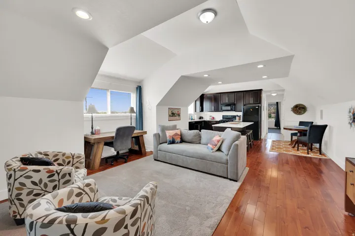 Open-concept living space with vaulted ceilings, recessed lighting, wood-finish flooring, and a kitchen featuring dark cabinetry and a central island with bar seating