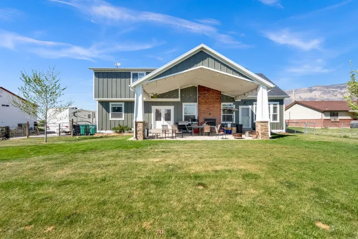 Expansive backyard with a covered patio, stone-wrapped columns, wood-paneled exterior accent, and double glass doors