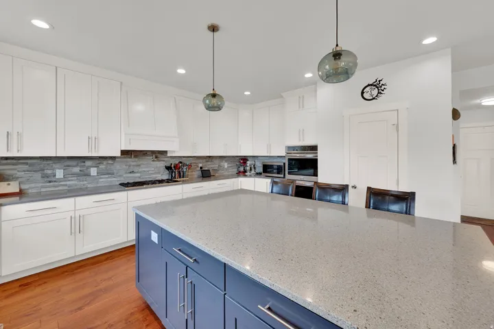 Kitchen featuring a large island with seating, white shaker-style cabinetry, stone countertops, a tile backsplash, and wood-finish flooring