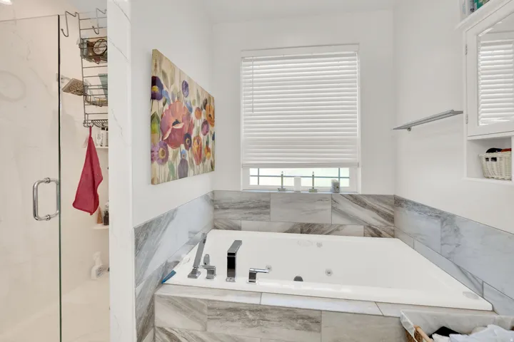 Jetted soaking tub with a tiled surround, a glass-enclosed shower, and a built-in medicine cabinet