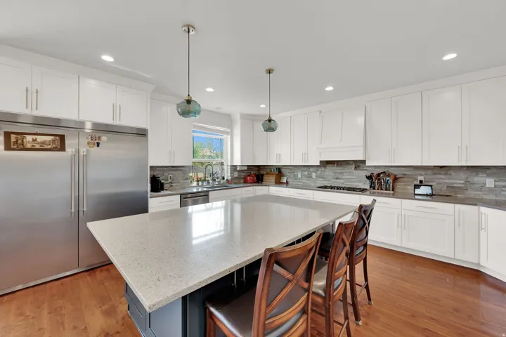 Expansive kitchen featuring a large central island, white cabinetry, integrated stainless steel appliances, wood-finish flooring, and a tiled backsplash