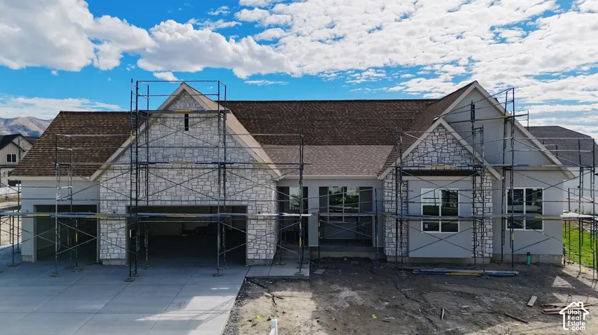 Single-story residential exterior featuring stone masonry, multi-gabled roofline with asphalt shingles, and concrete driveway