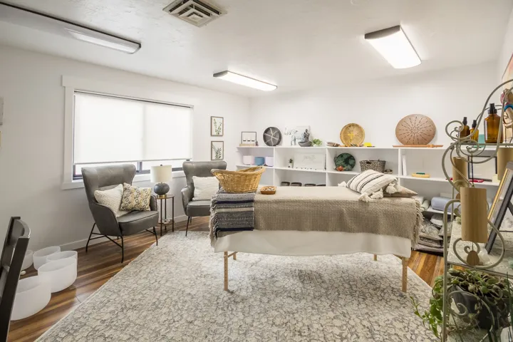 Bright, open living space featuring recessed and linear ceiling fixtures, large windows with natural light, wood-finish flooring, and built-in shelving with display niches