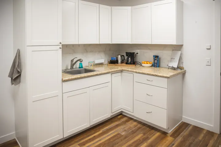 White shaker cabinetry, light-toned countertop, stainless steel sink, and wood-finish flooring