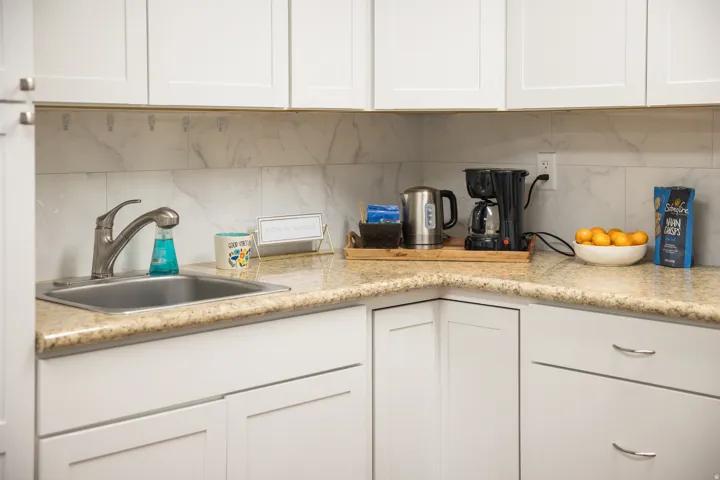 White cabinetry with brushed nickel hardware, light-toned countertop, stainless steel sink, and white tiled backsplash