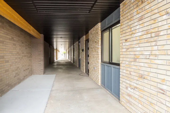 Covered walkway featuring a light-colored brick exterior, concrete flooring, and a dark soffit