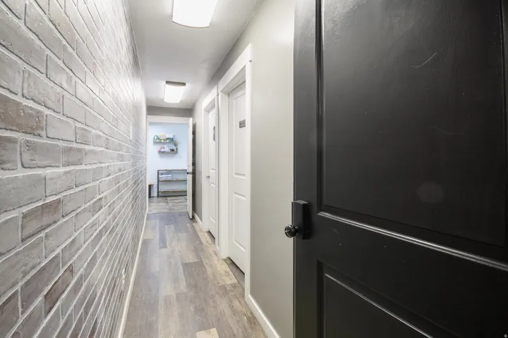 Hallway with wood-finish flooring, brick-patterned wall, flush-mount lighting, and solid-core panel doors