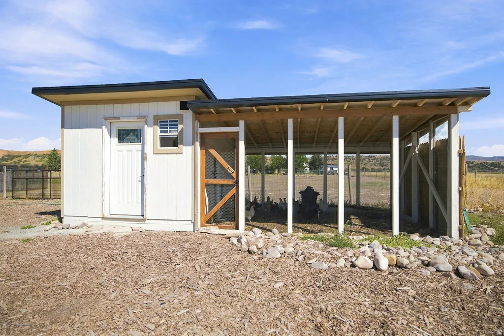 Outbuilding featuring an attached covered enclosure, white vertical siding, and a sloped roof