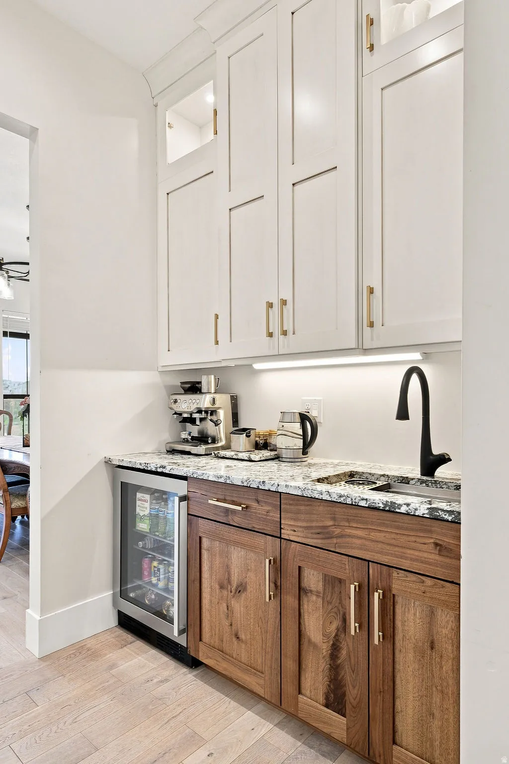 Two-tone cabinetry with upper white shaker-style cabinets and lower wood-finish cabinetry, under-cabinet lighting, natural stone countertop, and wood-finish flooring