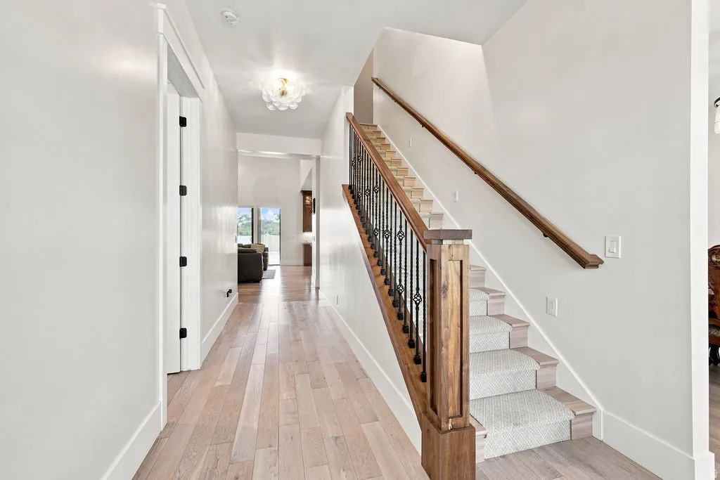 Wood-finish flooring, staircase with wood newel posts, wrought iron balusters, carpeted treads, and a contemporary ceiling fixture