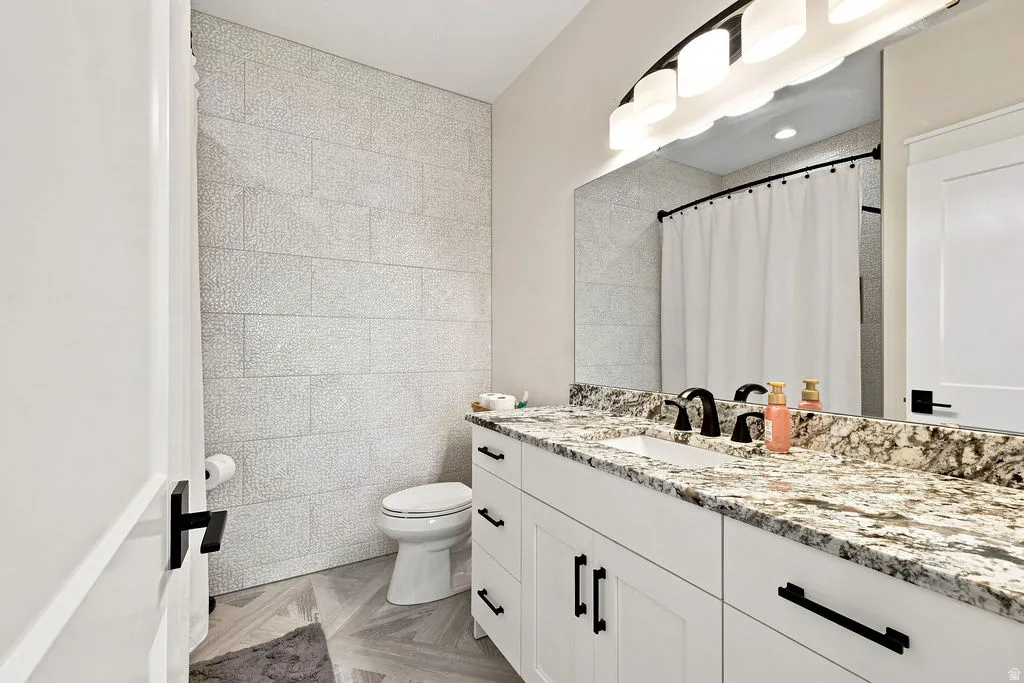 White shaker vanity with black hardware, integrated rectangular sink, speckled countertop, and large wall-mounted mirror