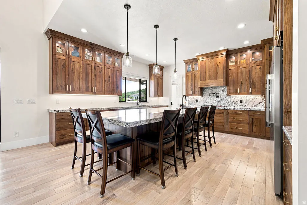 Wood-finish flooring, extensive wood cabinetry, generous center island with countertop seating, stone countertops, and stainless steel appliances