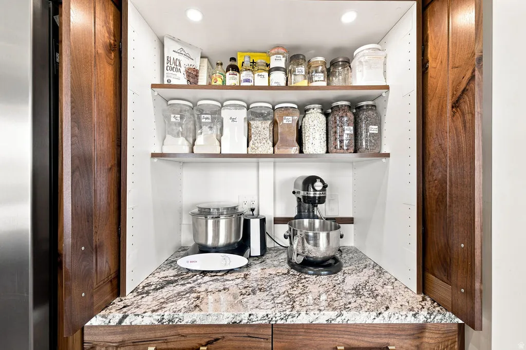Built-in pantry with wood cabinetry, granite countertop, adjustable shelving, and recessed lighting