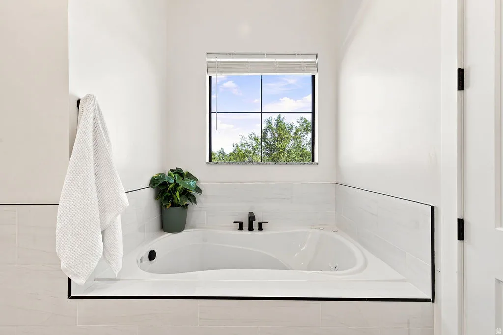 Built-in soaking tub with matte black fixtures, white tiled surround, and transom window