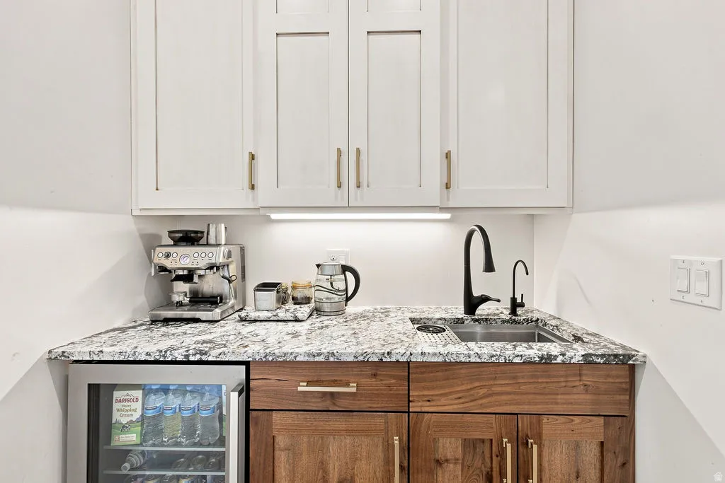 Built-in beverage refrigerator, undermount sink with matte black faucet, durable stone countertop, and custom cabinetry with gold-tone hardware