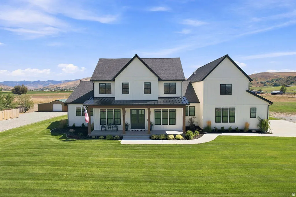 Modern farmhouse exterior with a covered porch, black framed windows, dark roof, and a gravel drive