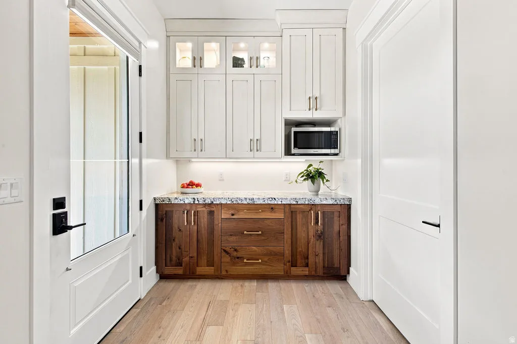 Light wood-finish flooring, two-tone cabinetry with upper glass-front cabinets, and a built-in microwave