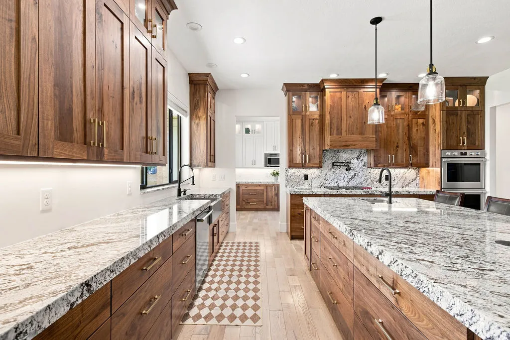 Spacious kitchen featuring extensive wood cabinetry, light-toned wood-finish flooring, two large islands with stone countertops, and recessed lighting