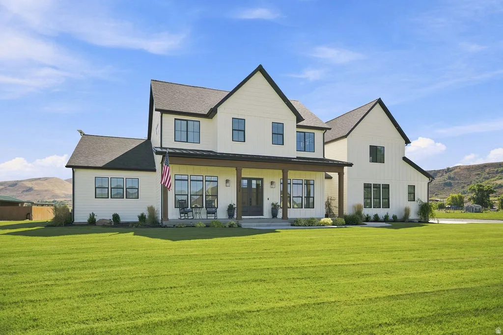 Modern farmhouse-style residence featuring a prominent covered porch, multiple dark-framed windows, and a dark shingle roof