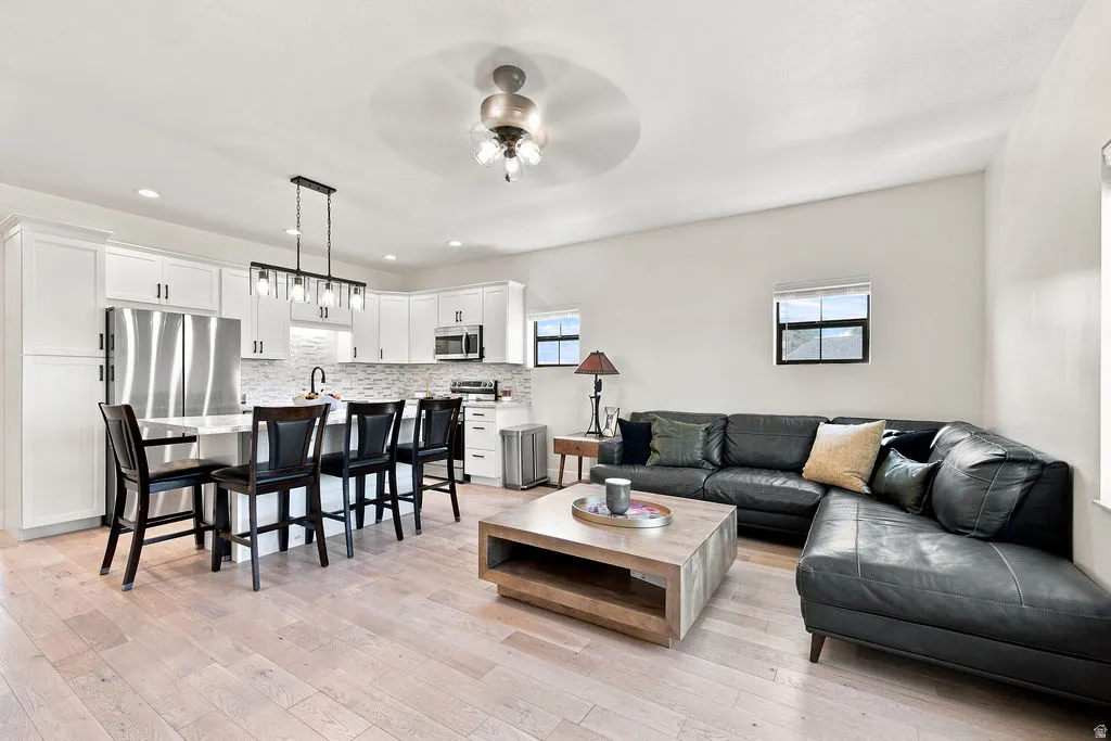 Light wood-finish flooring throughout, white cabinetry with stainless steel appliances, a kitchen island with seating, a tile backsplash, and recessed lighting