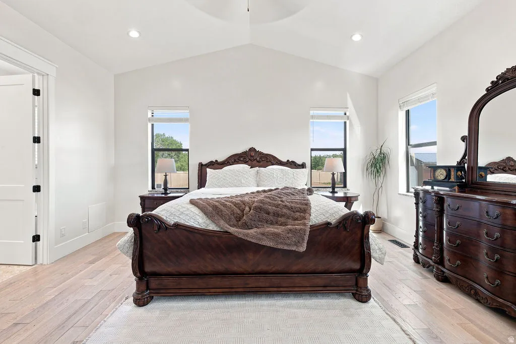 Vaulted ceiling with a central ceiling fan, light wood-finish flooring, recessed lighting, and two windows with roller shades