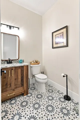 Patterned tile flooring, wood-finish vanity with gold-tone hardware, white countertop, modern rectangular mirror, and a wall-mounted light fixture