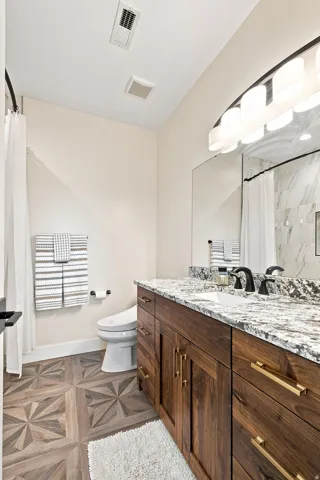 Wood-finish flooring with a geometric pattern, dark wood vanity with gold-tone hardware, white undermount sink, and a speckled stone countertop