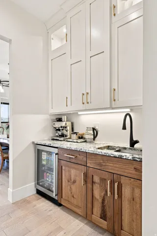 Two-tone cabinetry with upper white shaker-style cabinets and lower wood-finish cabinetry, under-cabinet lighting, natural stone countertop, and wood-finish flooring