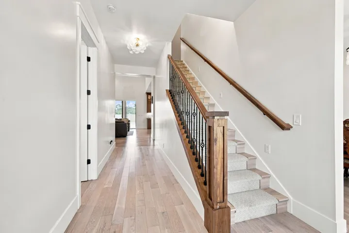 Wood-finish flooring, staircase with wood newel posts, wrought iron balusters, carpeted treads, and a contemporary ceiling fixture