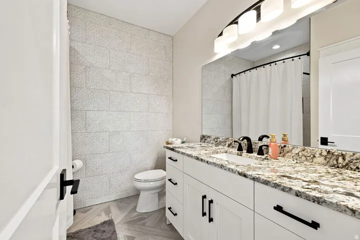 White shaker vanity with black hardware, integrated rectangular sink, speckled countertop, and large wall-mounted mirror