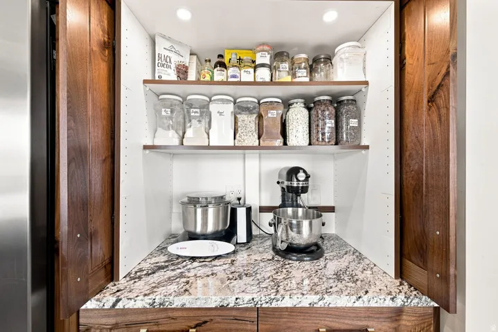 Built-in pantry with wood cabinetry, granite countertop, adjustable shelving, and recessed lighting