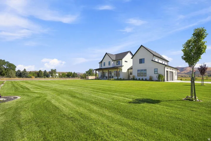 Contemporary farmhouse architecture with a covered porch, attached two-car garage, and expansive green lawn