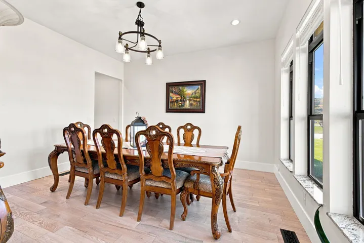 Wood-finish flooring, recessed lighting, and a multi-light chandelier illuminate this space, featuring multiple windows with sills
