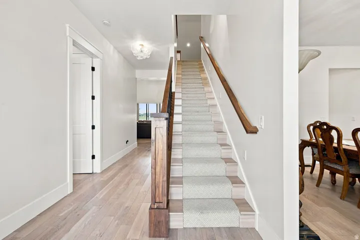Light wood-finish flooring, staircase with carpet runner, wood newel post and handrail, and a decorative ceiling light fixture
