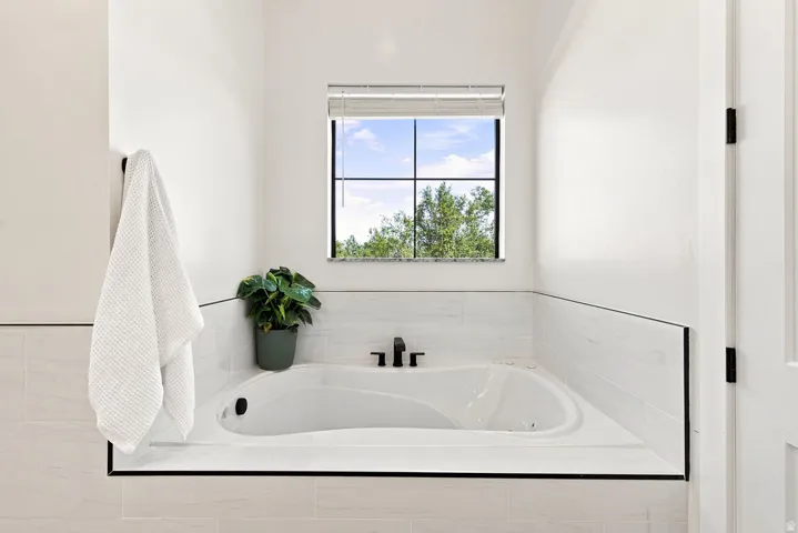 Built-in soaking tub with matte black fixtures, white tiled surround, and transom window