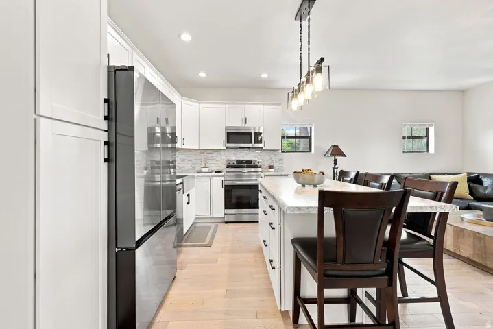 Modern kitchen featuring white shaker cabinetry, stainless steel appliances, a light-toned wood-finish floor, an island with countertop seating, and recessed lighting