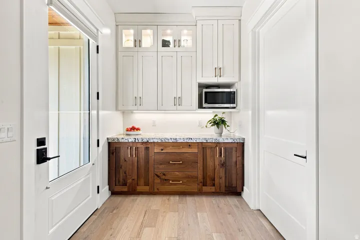 Light wood-finish flooring, two-tone cabinetry with upper glass-front cabinets, and a built-in microwave