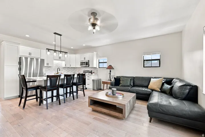 Light wood-finish flooring throughout, white cabinetry with stainless steel appliances, a kitchen island with seating, a tile backsplash, and recessed lighting