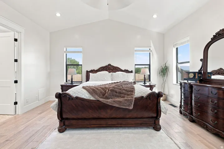 Vaulted ceiling with a central ceiling fan, light wood-finish flooring, recessed lighting, and two windows with roller shades