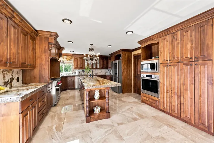 Spacious kitchen featuring extensive wood cabinetry, stone countertops, a large center island, built-in stainless steel appliances, and tiled flooring