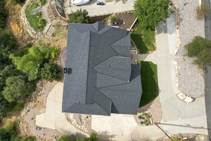 Asphalt shingle roof with multiple gables, extensive concrete driveway, and landscaped rock garden areas